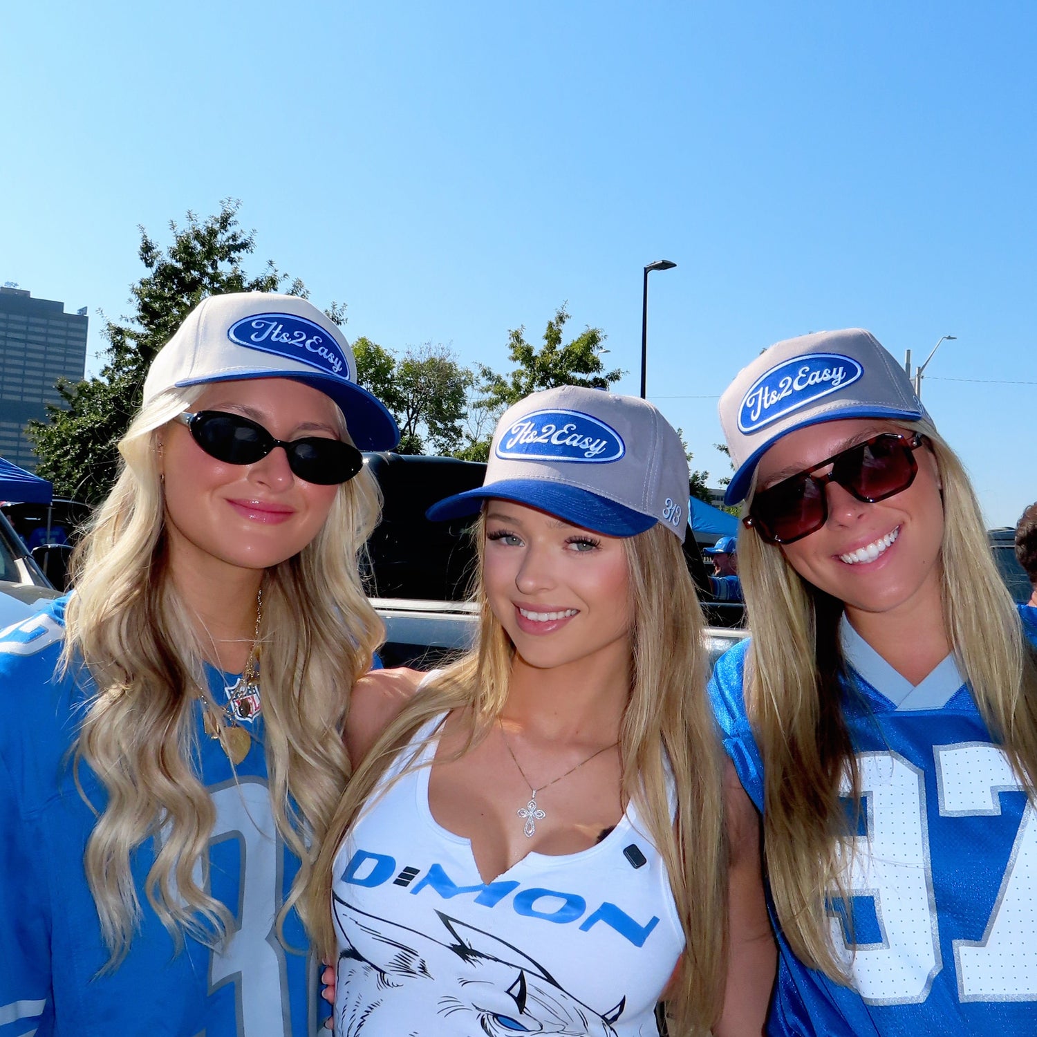 Three women in sports jerseys and hats standing outdoors on a sunny day.