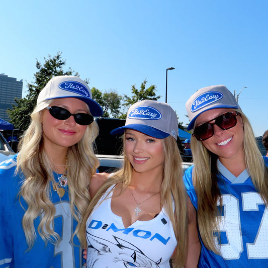 Three women in sports jerseys and hats standing outdoors on a sunny day.